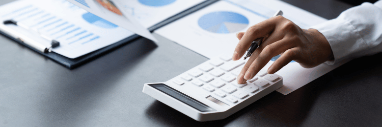 A person in a white shirt is analyzing printed graphs and charts while using a calculator.