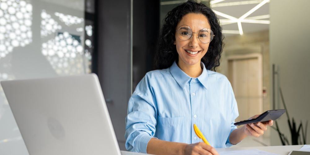 A smiling consultant analyzing data with a laptop and calculator, researching how much vCIO services cost for businesses.