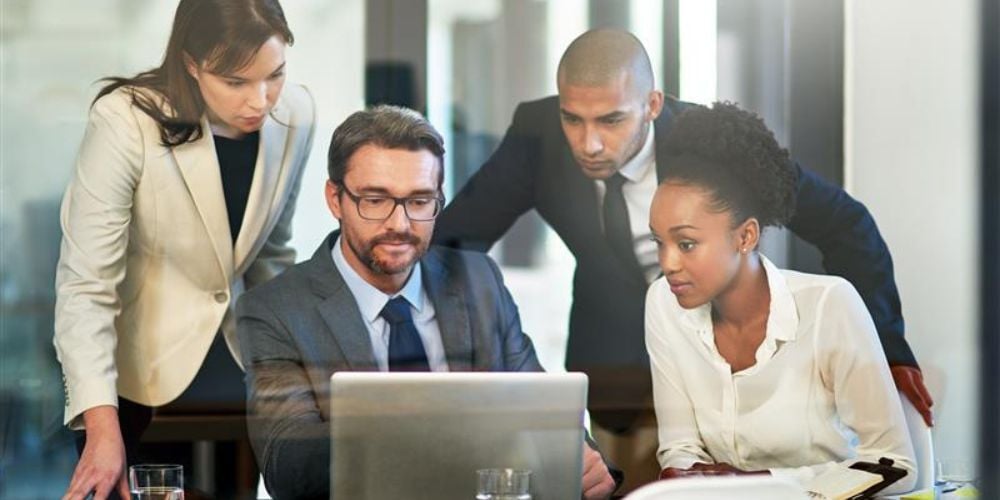 Business professionals analyzing data on a laptop during a meeting, reflecting the detailed review process behind CMMC audits and readiness assessments
