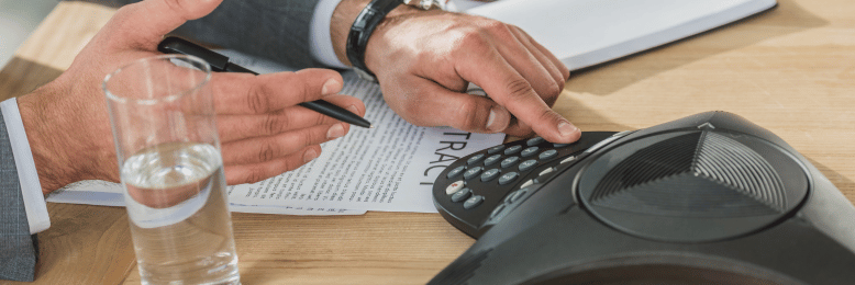Close-up of a businessman dialing on a conference phone, reviewing a VoIP contract