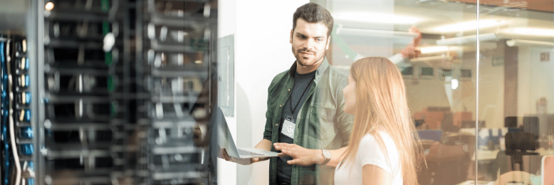 Colleagues discussing over laptop in server room, planning for Windows Server 2019 migration
