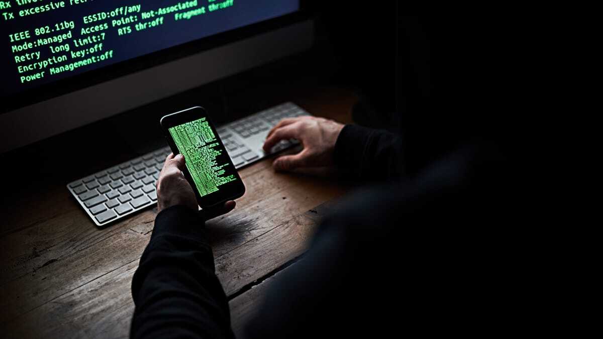 Hacker searching a phone and laptop for stolen passwords