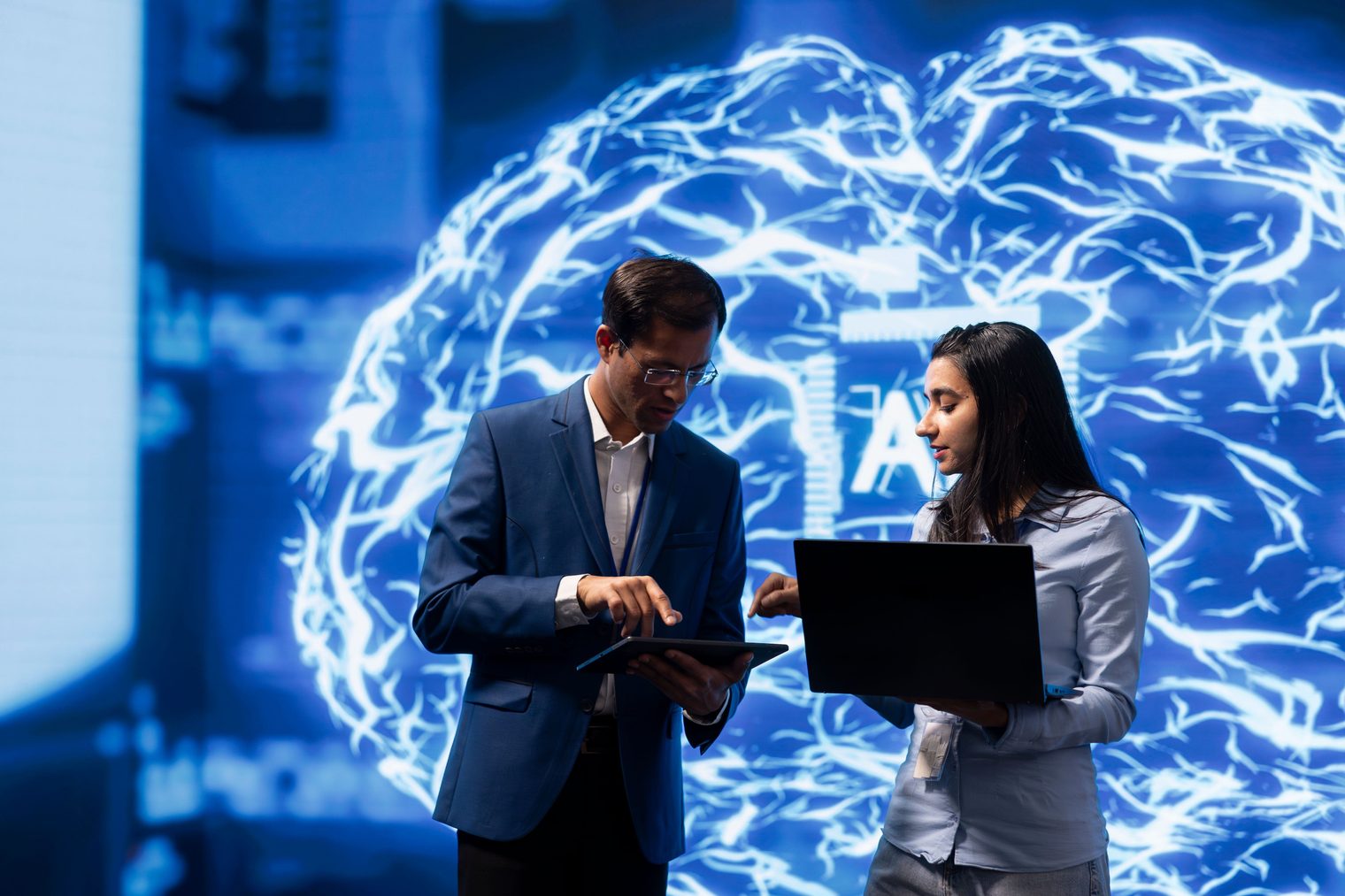 Two colleagues working together at a laptop in front of a large AI visualization, standing in for a company-wide AI rollout with training attached
