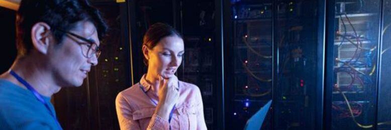 Male and female engineers analyzing infrastructure monitoring data on a laptop in a server room