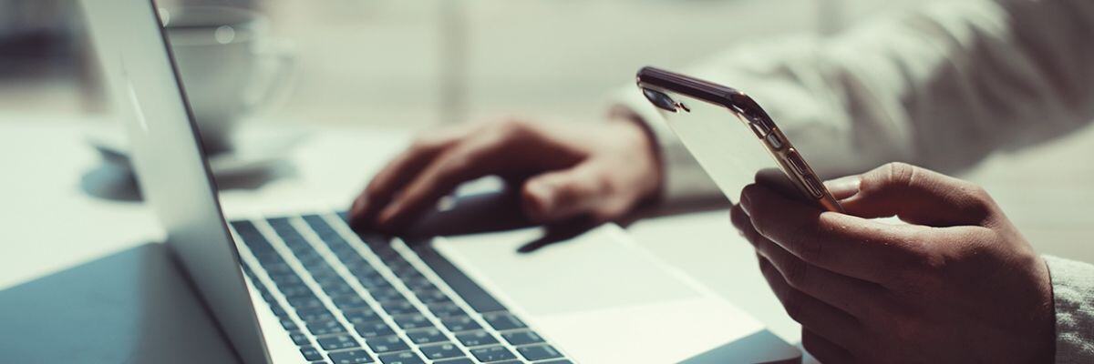 A person holding a phone and typing on a laptop