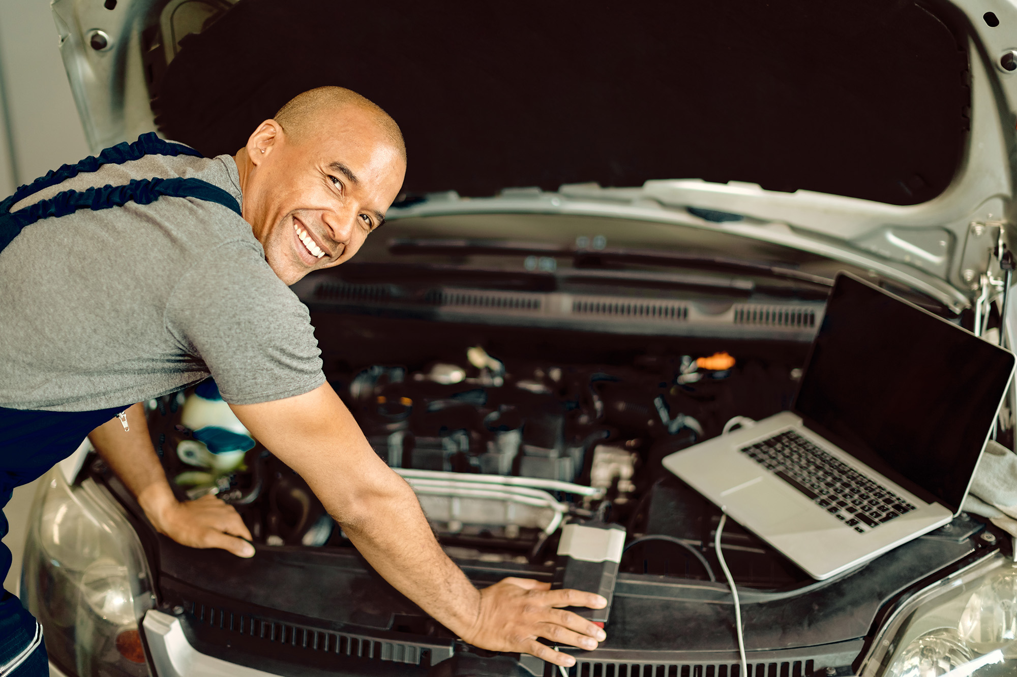 auto_when_yes (Happy mechanic working on engine diagnostic at car service workshop)