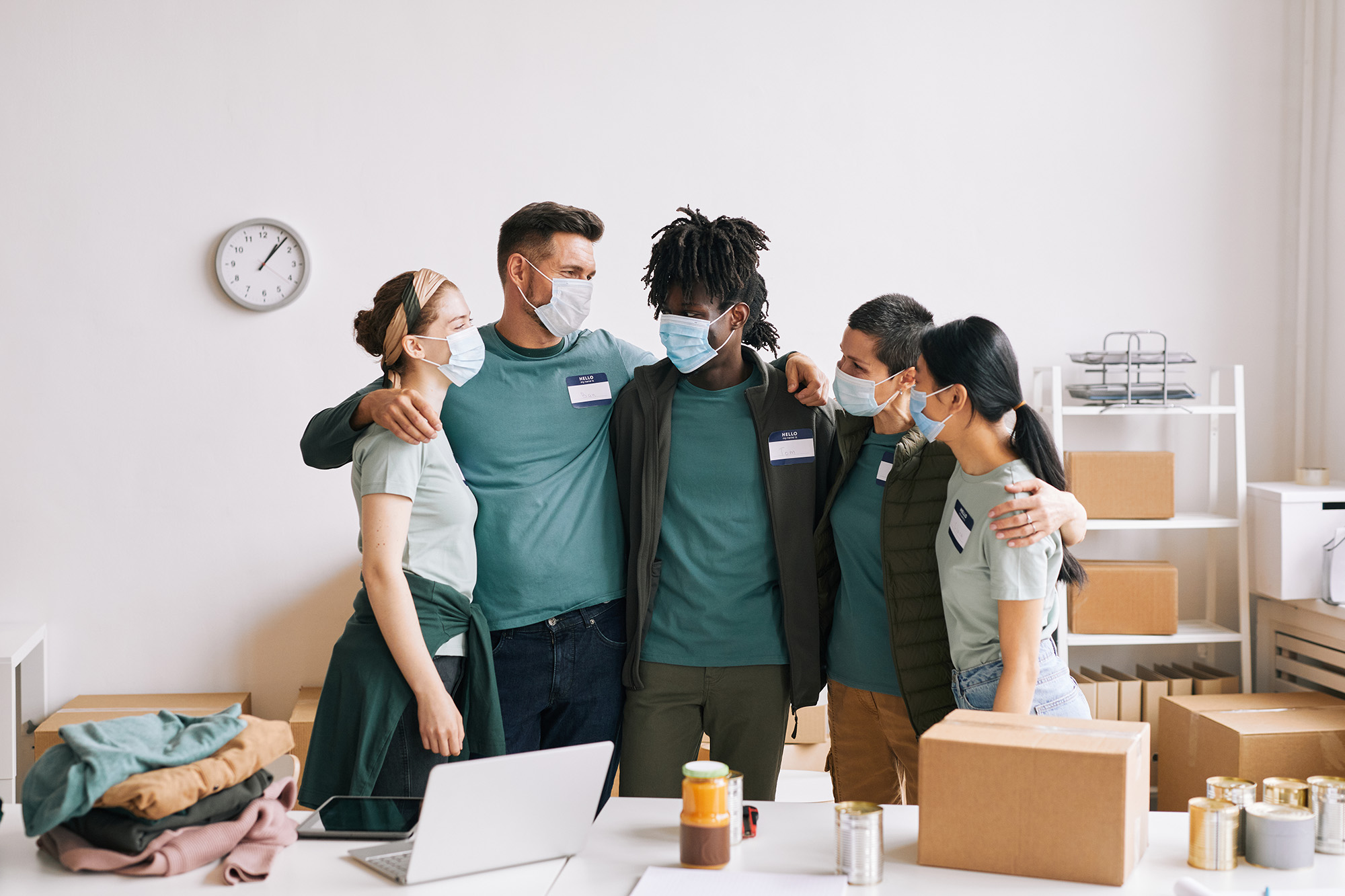 npo_when_yes (Diverse team of volunteers wearing masks while embracing at help and donation event)