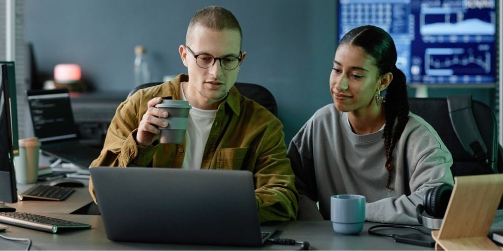 Two IT professionals reviewing security data on a laptop, discussing if SIEM is needed for their small business operations.
