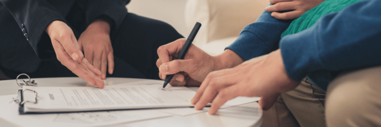 Two individuals are engaged in a discussion while one of them is signing a document.