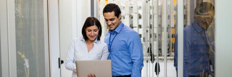 Two professionals discussing infrastructure data on a laptop in a data center environment
