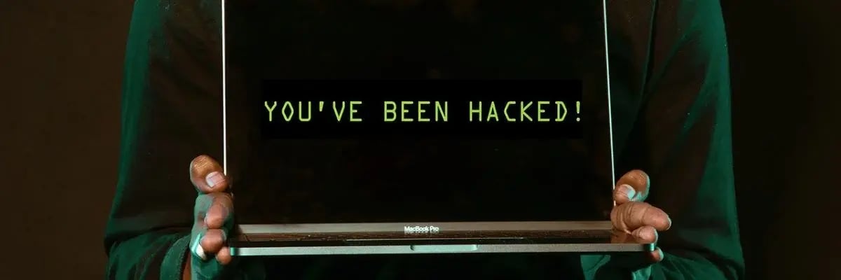 A person holding a laptop screen that displays the words 'YOU'VE BEEN HACKED!' in bright green text against a dark background, representing a cyberattack or data breach warning.