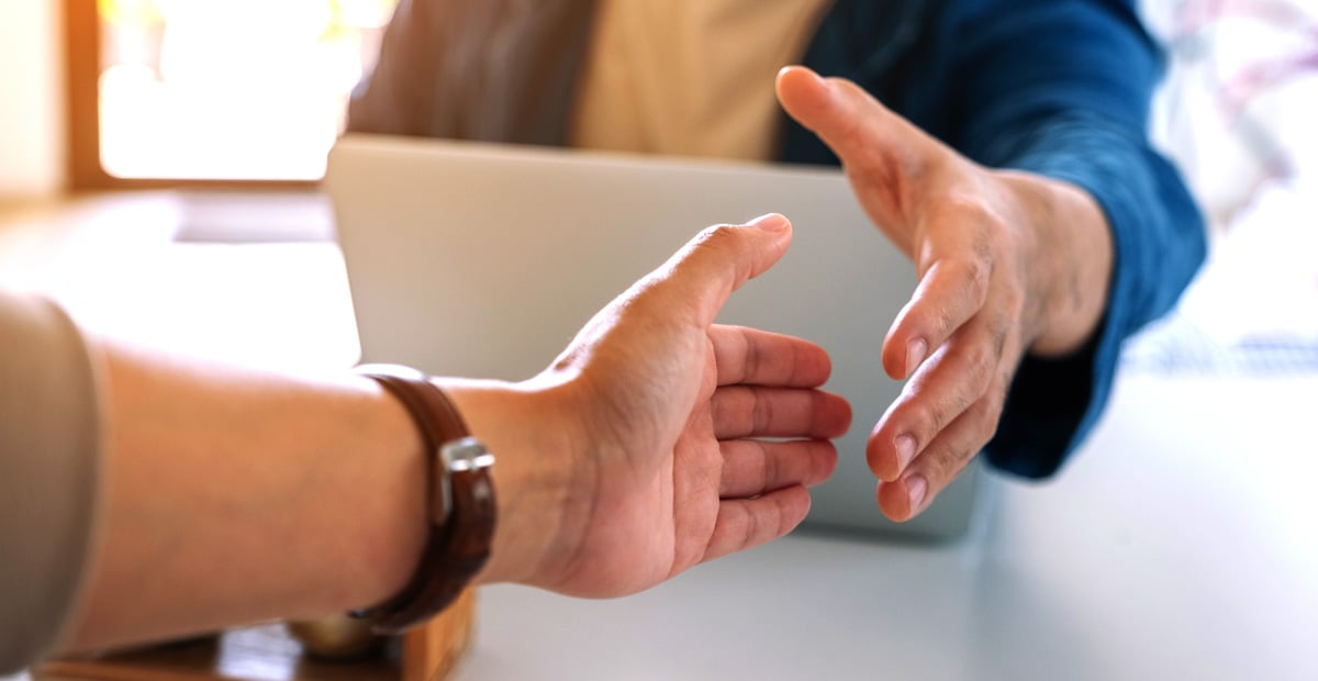 Two professionals reaching for a handshake over a desk, representing trust and choosing the right MSP partner for business IT.
