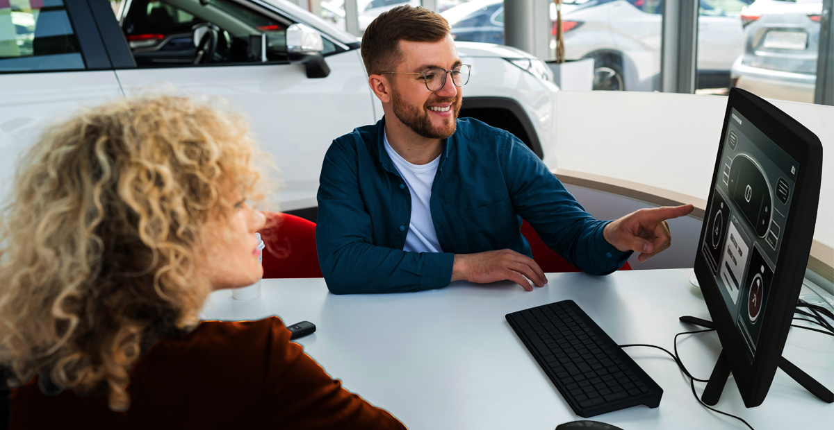 Car dealership staff reviewing vehicle information on a computer, representing managed IT support for automotive dealerships.