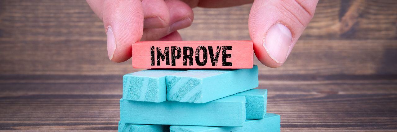 a person placing the final block of a pyramid with the word improve on it