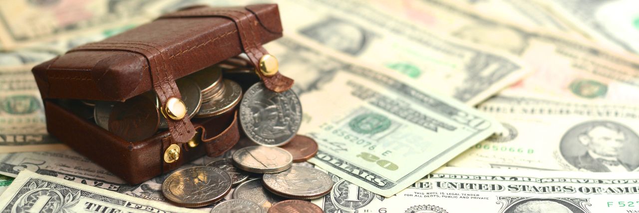 a briefcase of coins laying on paper bills depicting expensive