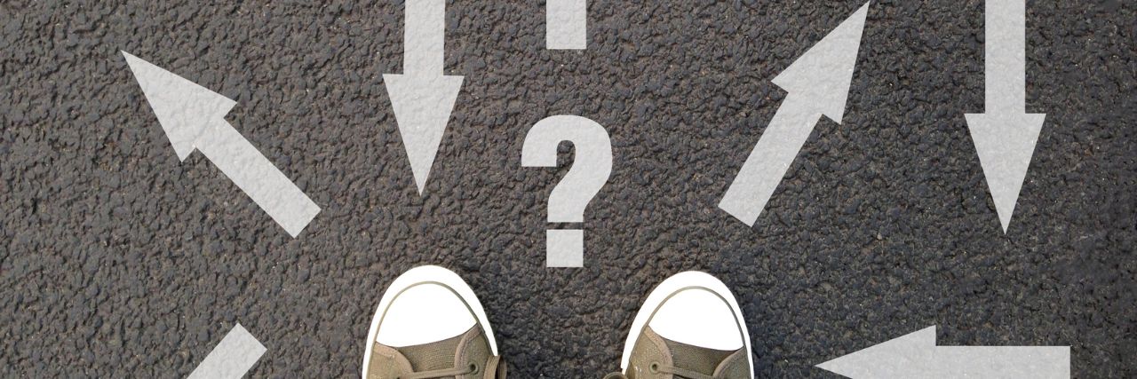 a pair of shoes facing a question mark and arrow signs painted on the road