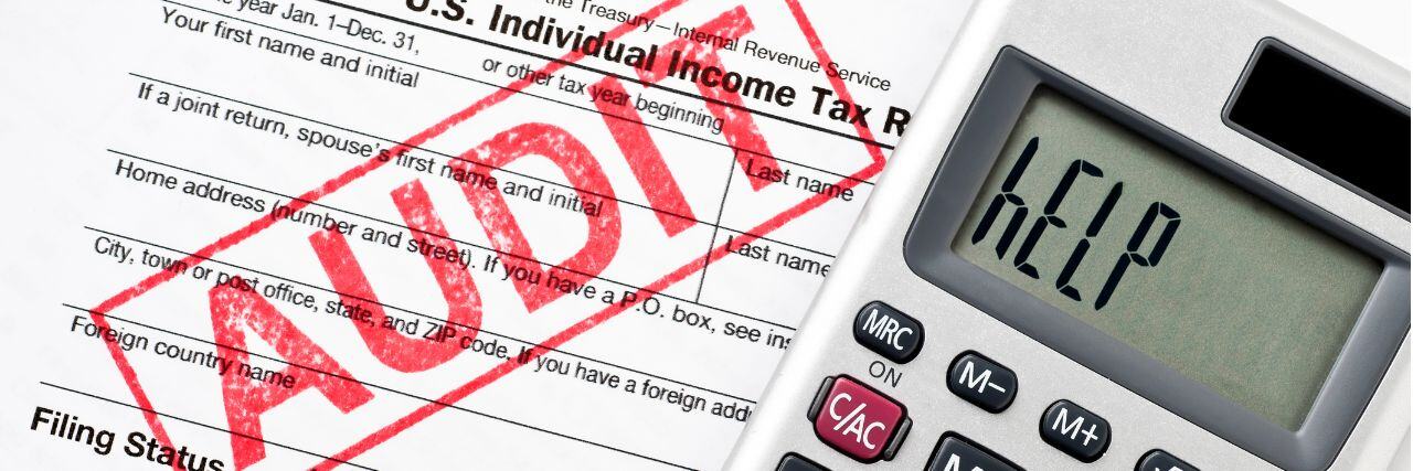 the word audit stamped with red ink on a paper with the word help written on a calculator beside it